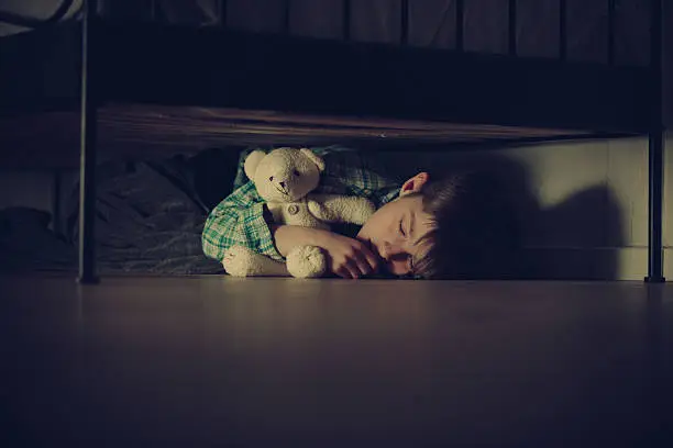Photo of Scared Boy Sleeping Under his Bed with Teddy Bear