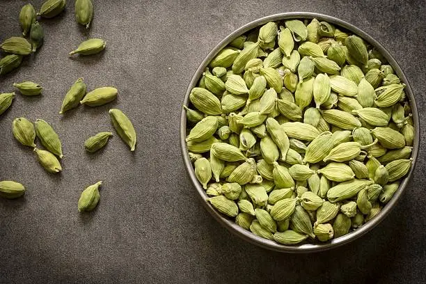 green cardamom pods in steel bowl with wooden background top view flat lay