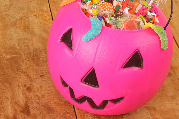 istock Pink plastic pumpkin filled with candy wooden table 518724193
