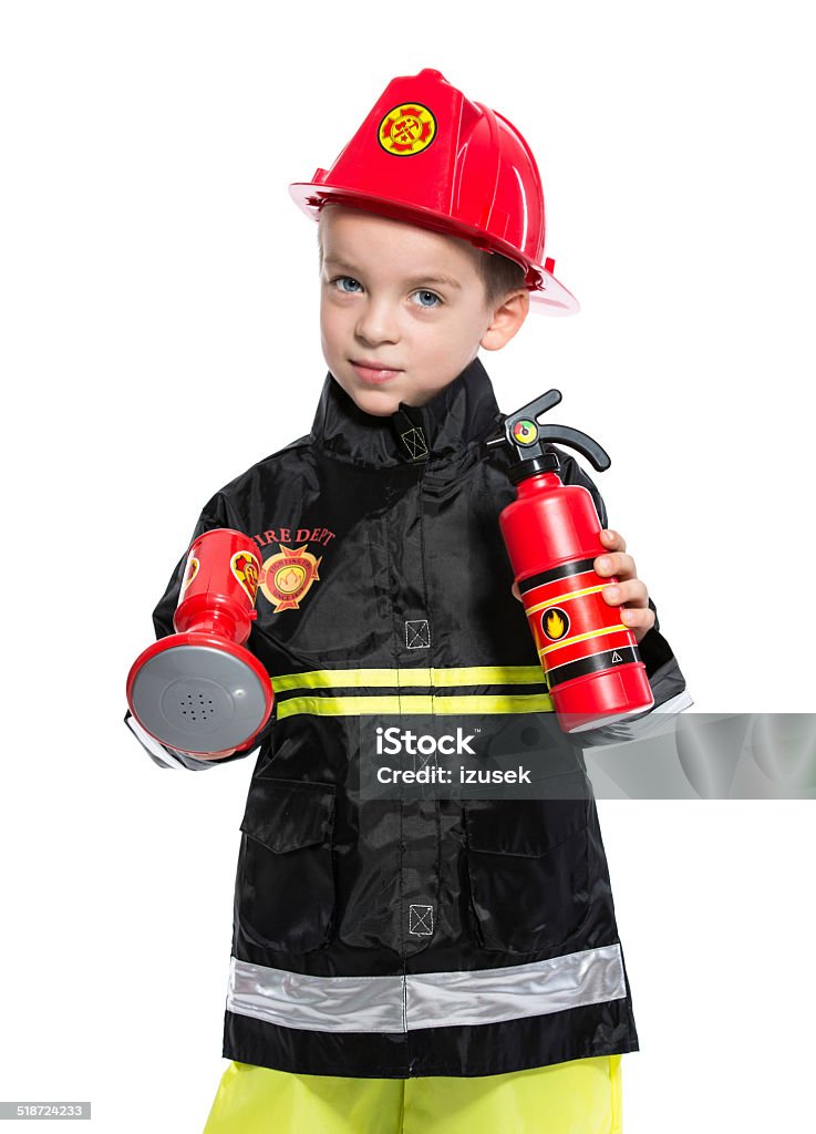 Junior Fireman Portrait of little boy dressed as a fireman, holding a toy fire extinguisher and smiling at camera. Studio shot, isolated on white. Child Stock Photo