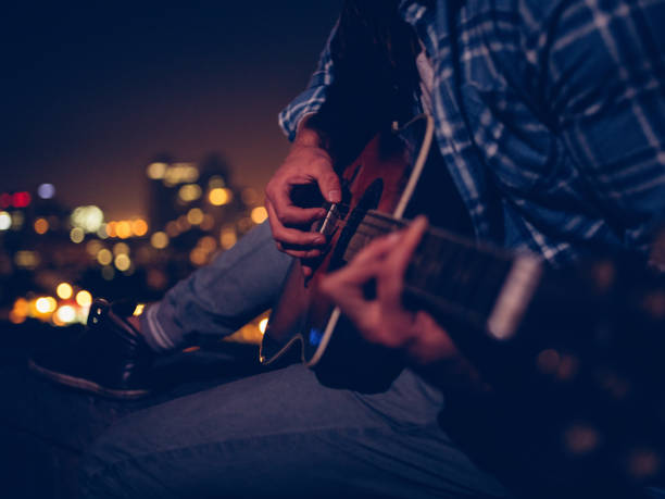 istock Young man playing guitar sitting on the rooftop at night 518727848