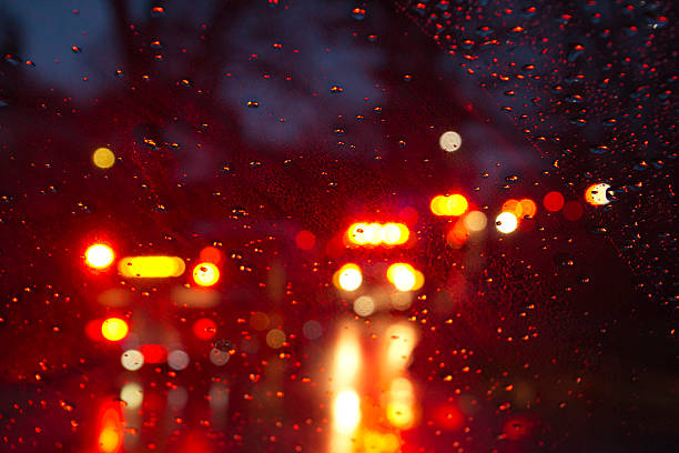 Flashing red and yellow lights of emergency vehicles and firetrucks seen on a rainy night through a wet car windshield