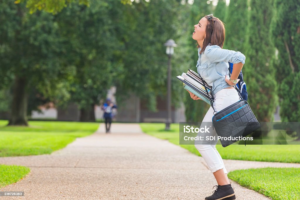 College student holding heavy books while walking on campus Pain Stock Photo