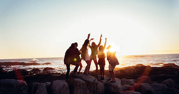 hipster et joyeux amis danser sur la plage au coucher du soleil - only teenage girls teenager adolescence sea photos et images de collection