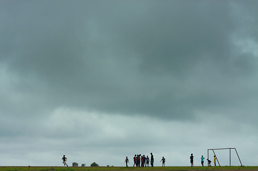Panchgani, MH, India - July 25, 2015: Kids playing football on flat plain with overcast sky. This is a monsoon season and still kids play football in rain; this is the charm of childhood. In this picture tried to capture the kids playing football and sky is overcast and almost about to rain.