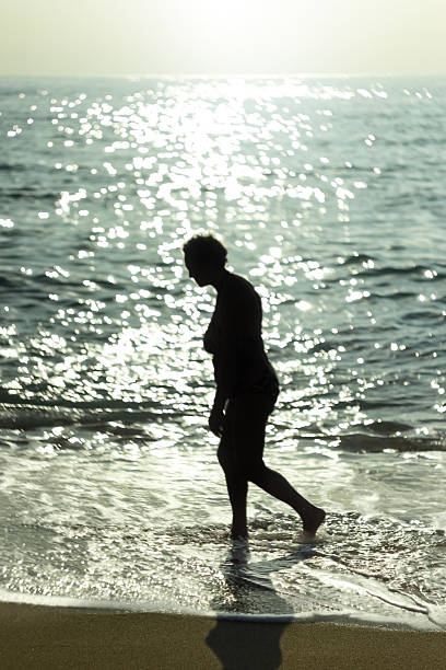 noir silhouette de femme marchant le long de la plage - shadow focus on shadow women sunset photos et images de collection