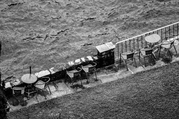 Tables and chairs on a terrace near a lake - black and white and grainy