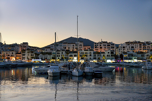 Puerto Banus Marina at night time. Taken just after sundown on a clear evening and showing some of the many boats reflected in the calm water. Beyond are some of the many shops bars and restuaraunts on the busy marina.