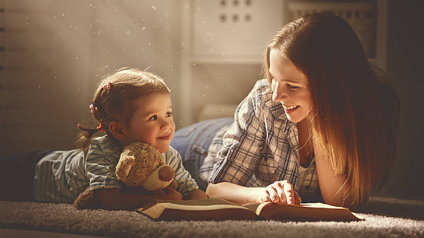 familia feliz madre con hija lea un libro en la noche - child bedtime imagination dark fotografías e imágenes de stock