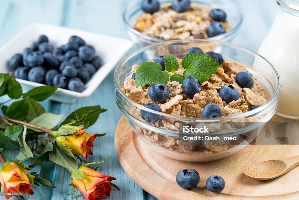 Breakfast with cereal, blueberry, milk and rose flowers Breakfast with cereal, blueberry, milk and rose flowers on a round wooden background 7-Grain Bread Stock Photo
