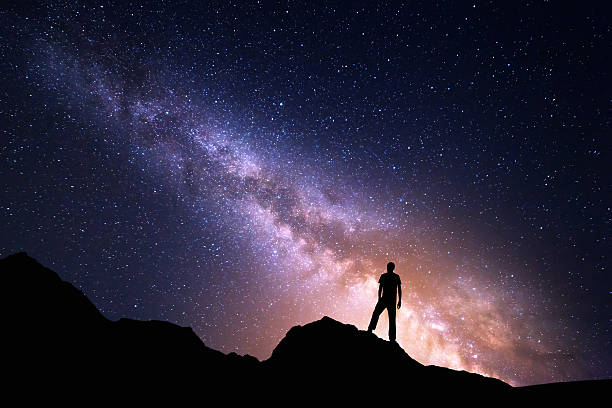 Landscape with Milky Way and silhouette of a happy man Landscape with Milky Way. Night sky with stars and silhouette of a happy man on the rock. Beautiful Universe. Space background climbing up a hill stock pictures, royalty-free photos & images