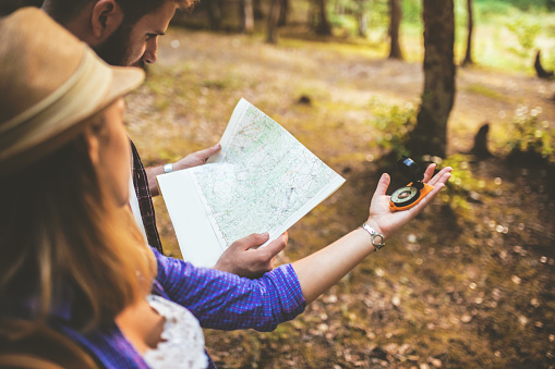 Happy couple going on a hike together in a forest. Man holding map and woman woman holding compass.