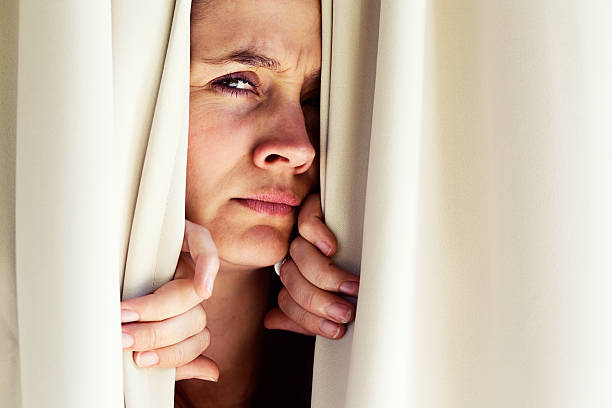 istock What's going on out there? Suspicious woman peeps through curtains 518779963