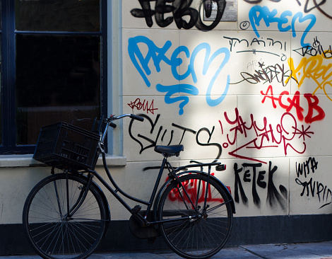 A black bike rests against an old white wall in Amsterdam, Holland, where various unknown/anonymous people have left their signatures in bold colors.