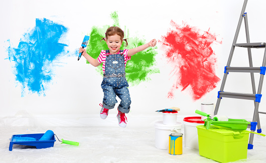 happy funny child girl doing repairs, jumping and paint the wall at home