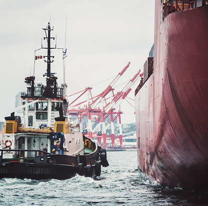 A container ship prepares to dock at a container port with the assistance of a tugboat.