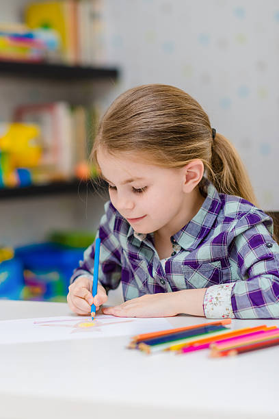 istock Cute smiling girl sitting at table drawing with multicolored pencils 518805708