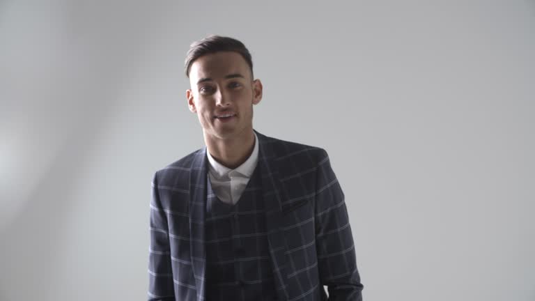 Young man in suit walks to camera, into focus, smiles, turns