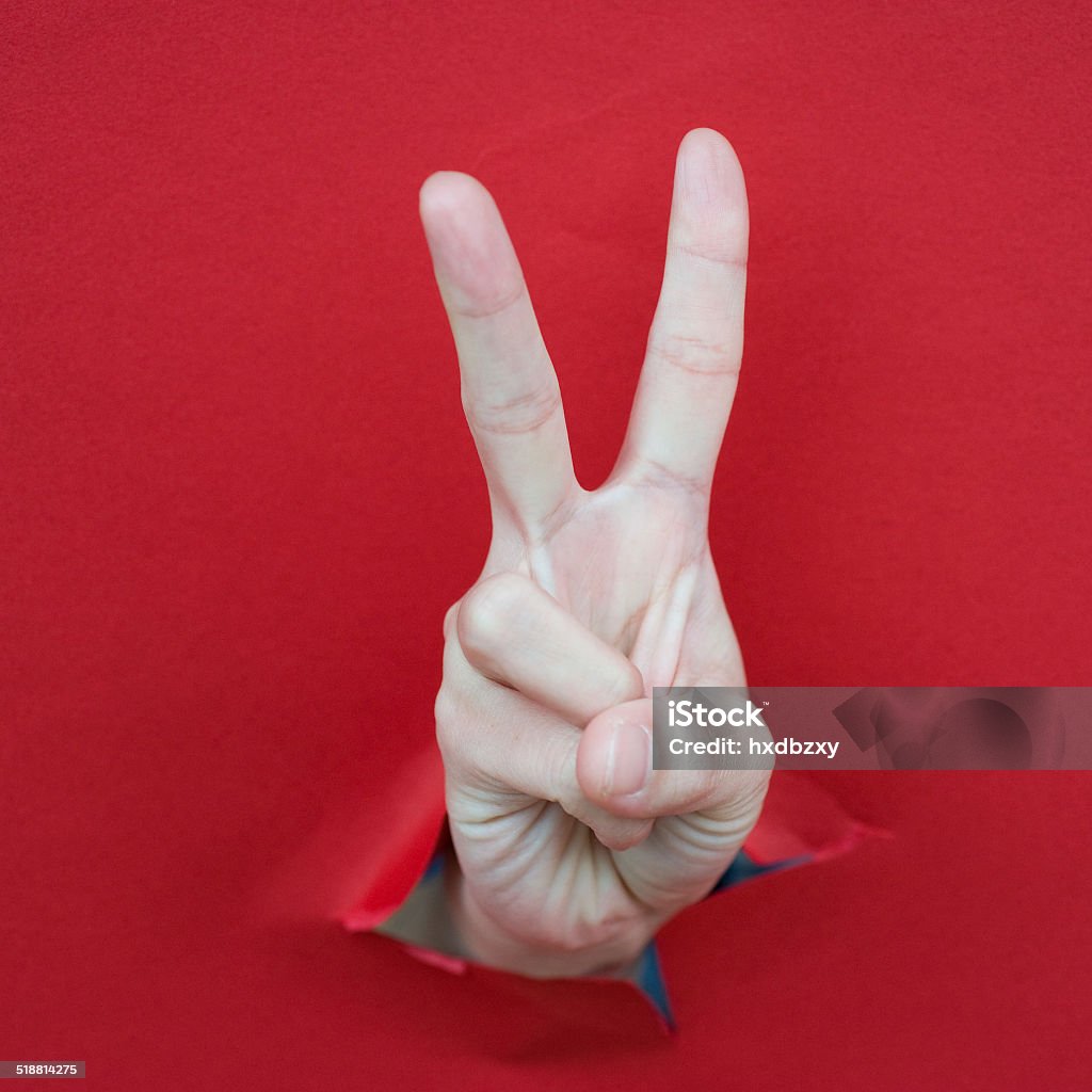 victory Hand of woman breaking through a paper wall pointing with the two fingers. Cut Or Torn Paper Stock Photo