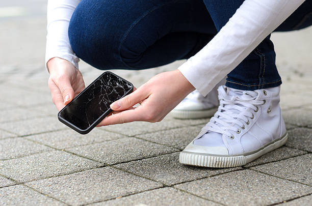 Kneeling person picking up broken phone on street Close up view on kneeling person in jeans and shoes picking up broken phone on stone paved sidewalk outdoors fracture stock pictures, royalty-free photos & images