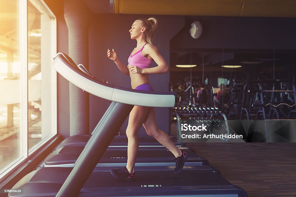 Fitness girl running on treadmill Fitness girl running on treadmill. Woman with muscular legs in gym Treadmill Stock Photo