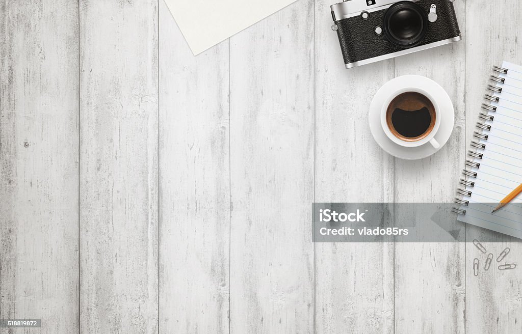 Office desk with free space for text. Camera, cup Office desk with free space for text. Camera, cup of coffee, paper, notepad, pencil on white wooden table. Top view. Desk Stock Photo