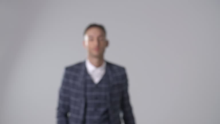 Smiling man in suit walks to camera, into focus, and turns