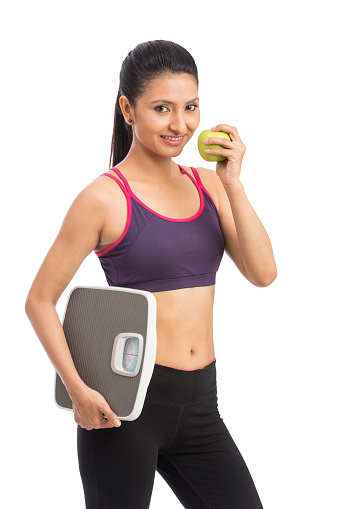 Indian attractive healthy diet eating woman with weighing scale and apple for weightloss