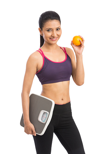 Indian healthy diet eating woman with scale and orange for weightloss