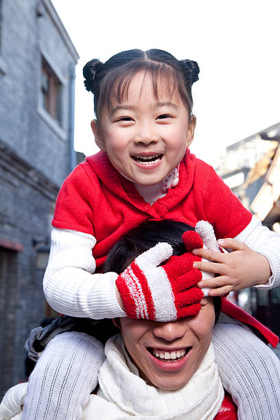 Inside their home, a Chinese family smiles as a mother in her thirties playfully places her one-year-old baby in a laundry tub, splashing water and sharing warm laughter. Shanghai, China. Spring.