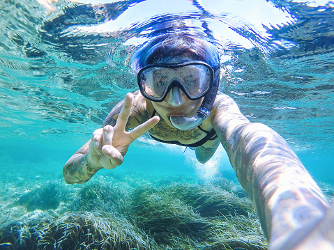 Young woman swimming with mask snorkeling in the Balearic Sea of Balearic Island. Showing victory signal.