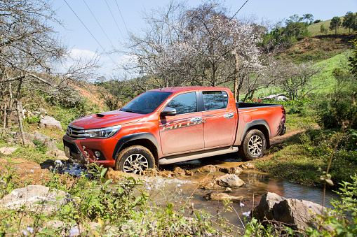 Hoabinh, Vietnam - Jan 10, 2016: The red New Toyota Hilux 2015 double cab 4x4 pickup truck crossing river and running on the mountain road in Vietnam. Japan-based car brand.