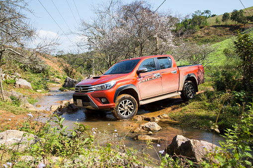 Hoabinh, Vietnam - Jan 10, 2016: The red New Toyota Hilux 2015 double cab 4x4 pickup truck crossing river and running on the mountain road in Vietnam. Japan-based car brand.