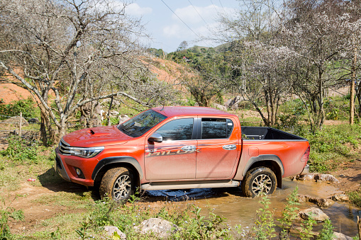 Hoabinh, Vietnam - Jan 10, 2016: The red New Toyota Hilux 2015 double cab 4x4 pickup truck crossing river and running on the mountain road in Vietnam. Japan-based car brand.