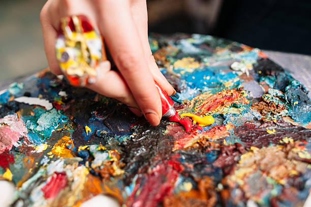 Painter mixes paint on the palette. Closeup Painter mixes yellow and red oil paint on the old palette. Closeup of paint mixing process in art workplace. Painter preparing to paint. oil paint palette stock pictures, royalty-free photos & images