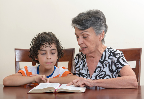 Grandmother teaching the Holy Bible to her grandson. Hispanic family studying the word of God in their daily Christian devotional. Reverence to God learning from His word.