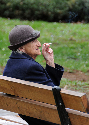 Veliko Tarnovo, Bulgaria - March 11, 2016: Aged Caucasian lady sits on the bench in the park and smokes a cigarette