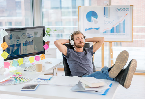 Creative business man relaxing at the office sitting on his desk and listening to music with earphones