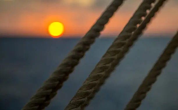 The sun sets behind the mainsheet on a sailing ship. 