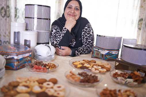 Shot of a mature muslim woman sitting in front of a variety of sweet cakes