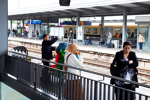 Essen, Germany - September 14, 2013: Capture and scene on platform of station Essen in Ruhrgebiet in summer. In foreground are some muslim and turk people. A woman with headscarf is drinking. At left side is cleaner of German Deutsche Bahn. At right side is an adult woman. In background are more people on other platforms.