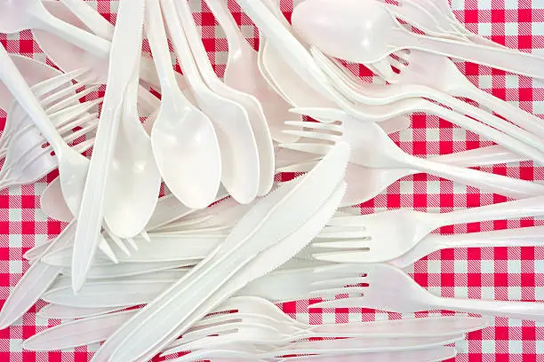 A jumble of white plastic forks, knives and spoons on a vinyl checkerboard tablecloth.