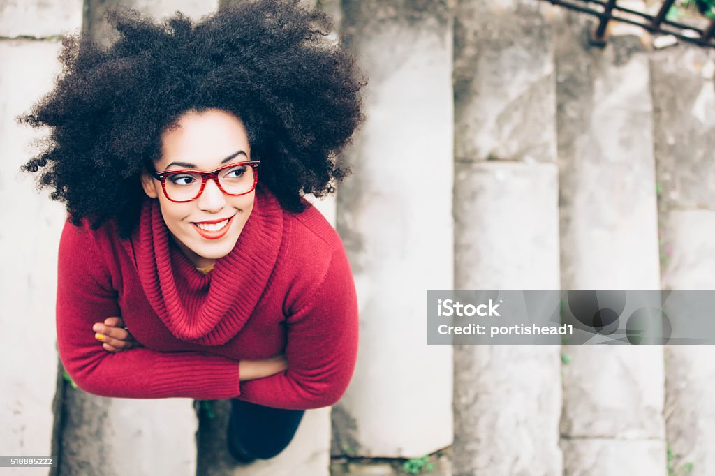 Portrait of smiling young woman standing on stairs Portrait of smiling young woman standing arm crossed on staircase. High angle view. Woman with curly hair, red eyeglasses, and red pullover. Red Stock Photo
