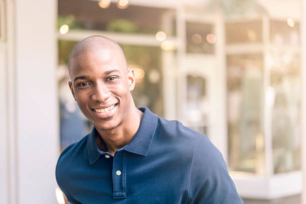 joven hombre sonriendo en el exterior tienda - polo shirt african ethnicity men african descent fotografías e imágenes de stock