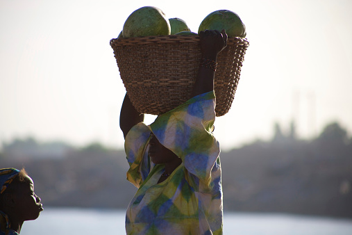 Mopti, Mali - December 26, 2010: Unidentified Woman carrying vegetables on her head in the streets of Mopti with a young girl looking at her, 2010