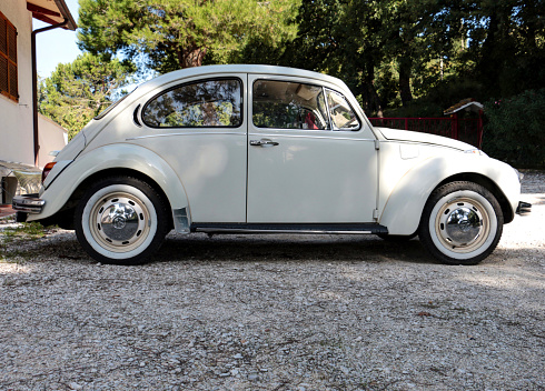 Ancona, Italy - October 12, 2014: Side view of a white Volkswagen Beetle produced in 1971 parked near a country house. It is certainly the most well-known German automobile in the world, a symbol of the rebirth of German industry after World War II, and the first Volkswagen model ever.