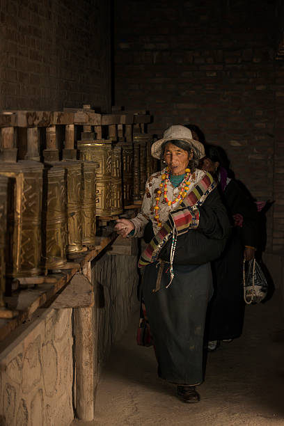 Langmusi, Tibet, Сhina - September 16, 2014: Old Tibetan woman is walking and turning prayer wheels in a dark room of  the monastery of Langmusi, Gansu, China, in the former Tibetan region of Amdo. Langmusi sits on the border between Gansu and Sichuan provinces.