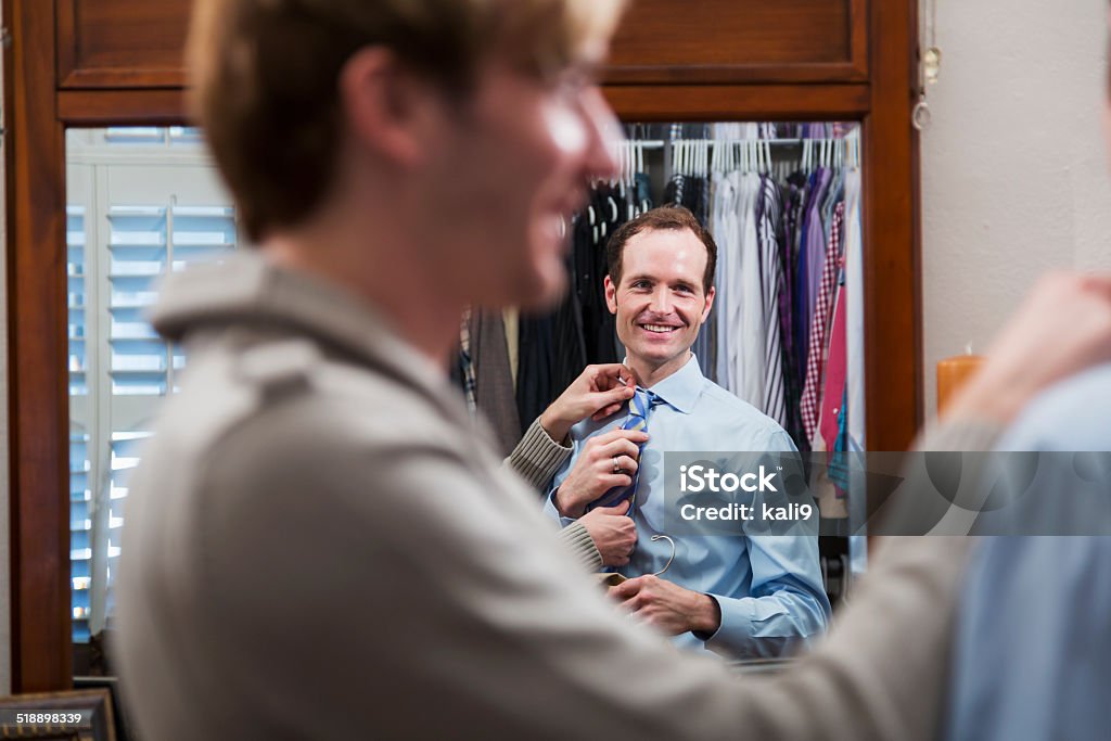 Gay couple getting dressed Homosexual couple (20s, 30s) at home, in closet.  Man helping partner get dressed for work. Necktie Stock Photo