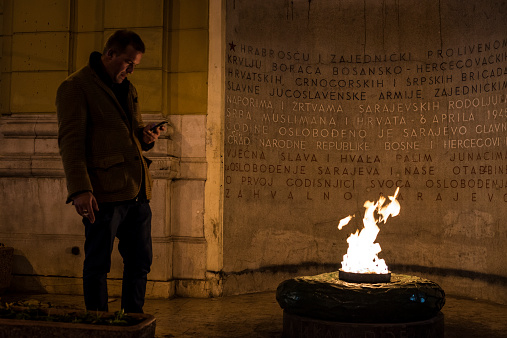 Sarajevo, Bosnia and Herzegovina - October 6, 2013: A man checks his phone at the eternal flame in Sarajevo, Bosnia and Herzegovina. The flame is a memorial dedicated in 1946 to the military and civilian victims of the Second World War in Sarajevo.