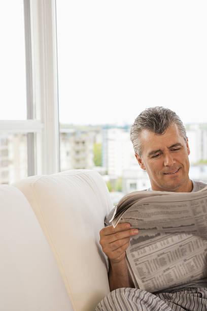 istock Middle-aged man reading newspaper on sofa 518898858